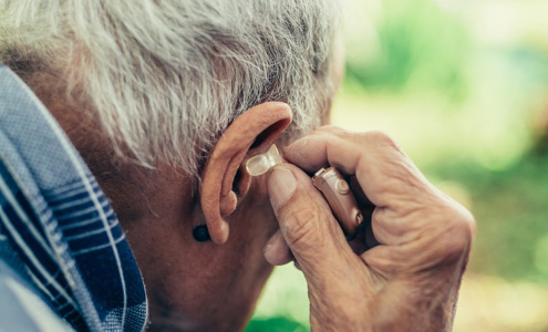 An elderly man puts in his hearing aid